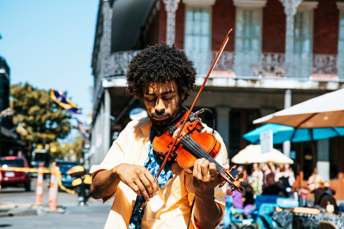 A man in the streets of a rustic town, it could be New Orleans, playing a violin.